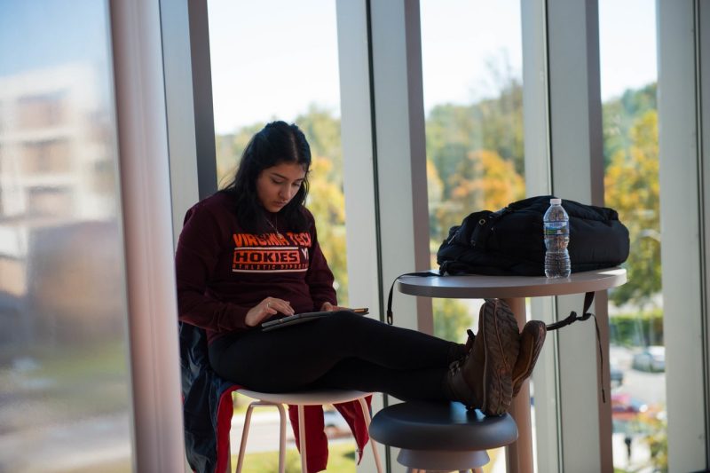 female student works with tablet at tall table with glass wall background